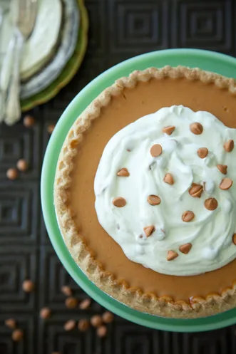 Paula Deen butterscotch pie in a pie shell topped with whipped cream and butterscotch morsels on a green cake stand
