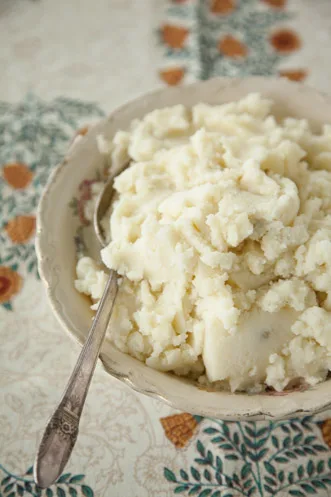 Paula Deen buttery buttermilk mashed potatoes piled in a vintage bowl with a silver spoon on a floral tablecloth