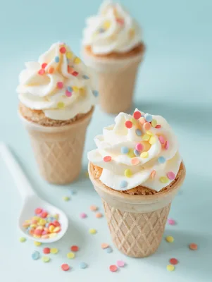 Paula Deen cake ice cream cones topped with swirls of white frosting and colorful confetti sprinkles