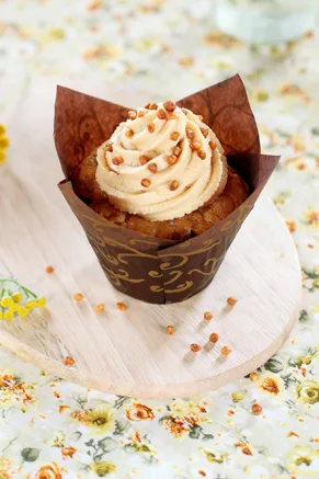 Paula Deen caramel frosting piped in a swirl on a cupcake in a brown wrapper, topped with golden toffee bits