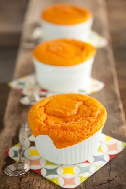 Paula Deen carrot souffle baked in white ramekins with golden orange puffed tops on a rustic wooden board