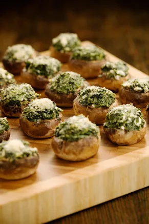 Paula Deen cheese stuffed mushrooms topped with spinach and Parmesan on a wooden cutting board