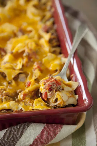 Paula Deen cheeseburger casserole with melted cheddar and egg noodles in a red baking dish with a serving spoon