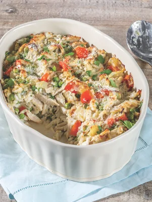 Paula Deen cheesy chicken and rice casserole in a white oval baking dish with peas, red bell pepper and fresh parsley on top