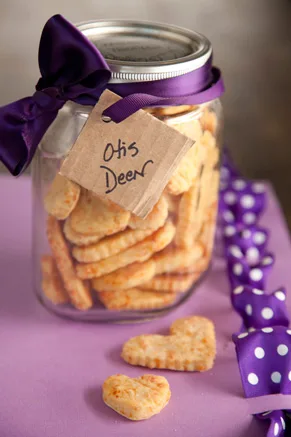 Paula Deen cheesy dog treats, golden heart-shaped cheese biscuits in a glass jar tied with a purple ribbon and an Otis Deen tag