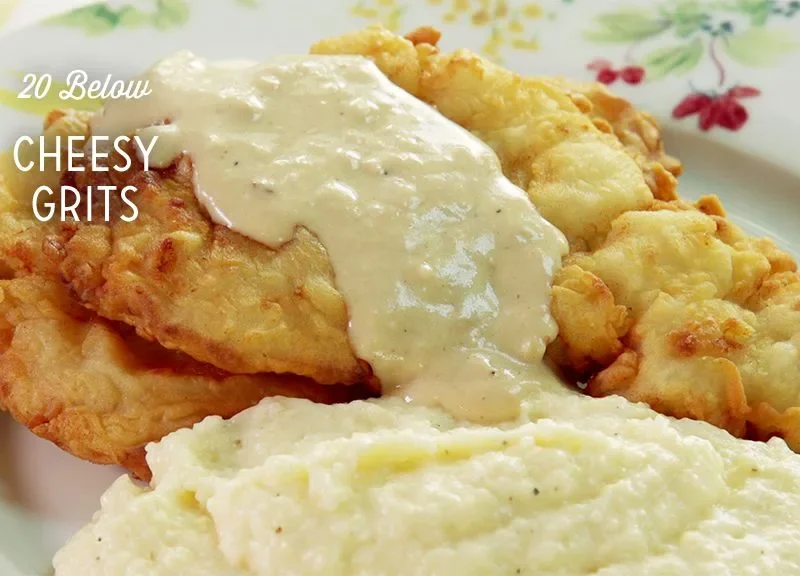 Paula Deen cheesy grits served in a creamy mound on a floral plate beside golden fried chicken topped with gravy