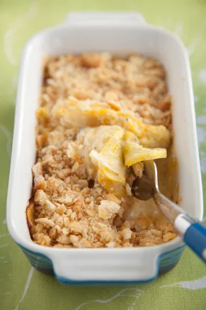 Paula Deen cheesy squash casserole in a white baking dish with a golden cracker topping and a serving spoon lifting out tender yellow squash
