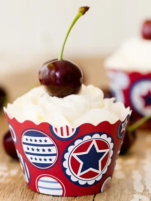 Paula Deen cherry cobbler cupcakes topped with fresh whipped cream and a stemmed cherry in a red, white and blue star cupcake wrapper
