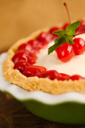 Paula Deen cherry cream cheese pie in a green pie dish with a graham cracker crust, creamy filling and glossy cherries topped with a mint sprig