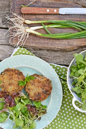 Paula Deen chicken croquettes with Creole sauce, two golden pan-fried patties on a plate with fresh salad greens beside green onions