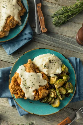 Paula Deen chicken-fried steak with cream gravy served with Brussels sprouts and mashed potatoes on a teal plate