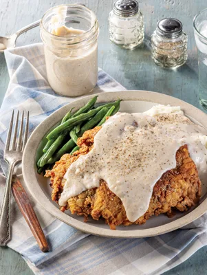 Paula Deen chicken-fried steak with milk gravy served on a plate with green beans and mashed potatoes