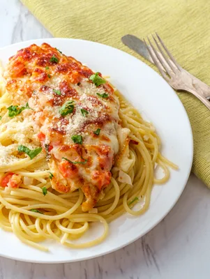 Paula Deen chicken parmesan with melted mozzarella and marinara over spaghetti on a white plate with parsley