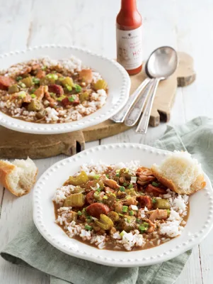 Paula Deen chicken, sausage, and okra gumbo served over rice in white bowls with green onion and crusty bread