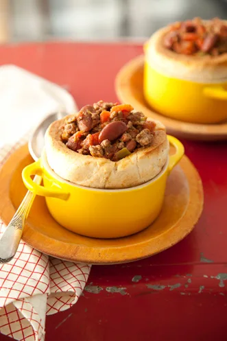 Paula Deen chili in a biscuit bowl served in a yellow ramekin with beans, ground beef and diced peppers