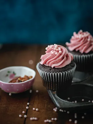Paula Deen chocolate birthday cupcakes with vanilla frosting swirled pink and topped with pearl sprinkles on a wooden table