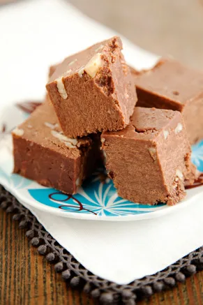 Squares of Paula Deen chocolate cheese fudge with chopped nuts stacked on a blue and white plate