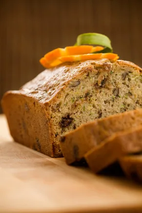 Paula Deen chocolate chip zucchini bread loaf sliced on a wooden board topped with orange zest ribbons and a zucchini slice