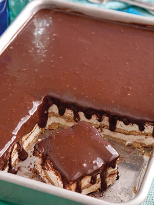 Paula Deen chocolate-hazelnut éclair cake in a baking dish with a glossy chocolate topping and one square lifted out showing the graham cracker and pudding layers