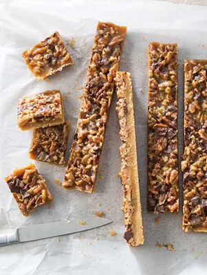 Paula Deen chocolate pecan pie bars cut into squares and long strips on parchment paper with a knife beside them