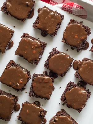 Paula Deen chocolate Sybil cake cut into squares with glossy pecan fudge frosting on a white platter