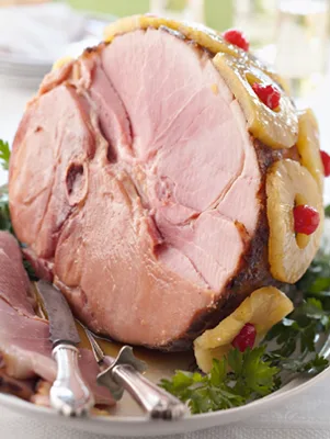 Paula Deen classic holiday baked ham with glaze, pineapple rings and maraschino cherries on a platter with fresh herbs