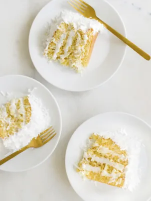 Three slices of Paula Deen coconut and lemon curd cake on white plates with gold forks, showing layers of cake, lemon curd and shredded coconut