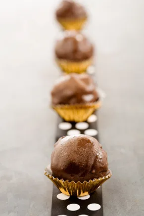 Paula Deen cookie dough truffles dipped in chocolate sitting in gold candy cups in a row