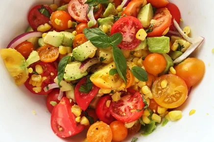 Paula Deen corn, avocado and tomato salad with halved cherry tomatoes, corn kernels, diced avocado, red onion and fresh basil in a white bowl