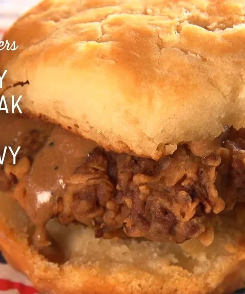 Paula Deen country fried steak with milk gravy served on a split buttermilk biscuit over a colorful striped napkin