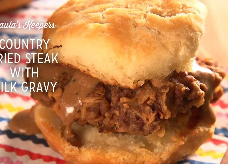 Paula Deen country fried steak with milk gravy served on a split buttermilk biscuit over a colorful striped napkin