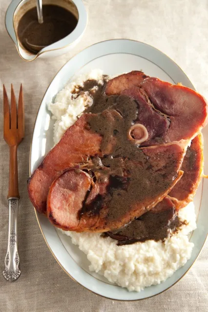 Paula Deen country ham and red-eyed gravy with sliced ham steaks over creamy white grits on a white oval platter