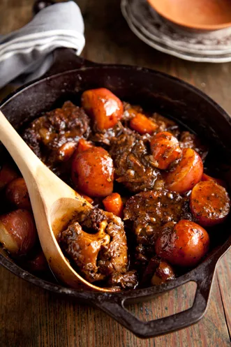 Paula Deen country oxtails braised with red potatoes and carrots in a cast iron pot with a wooden spoon