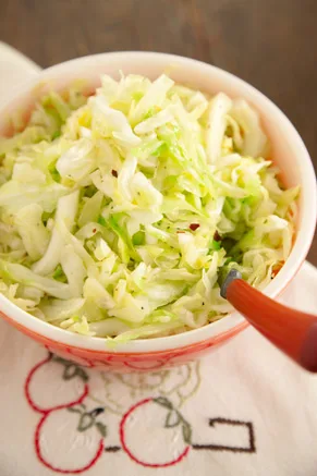 Paula Deen country style fried cabbage with red pepper flakes served in a red and white bowl with a wooden spoon