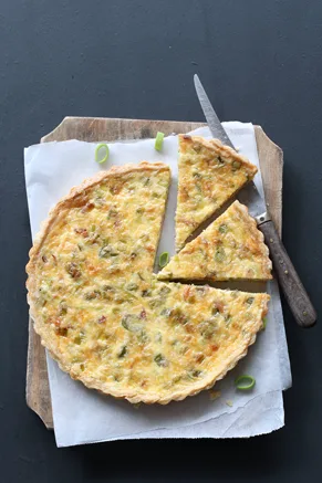 Paula Deen crab quiche in a golden crust with two slices cut and scallion pieces on parchment paper