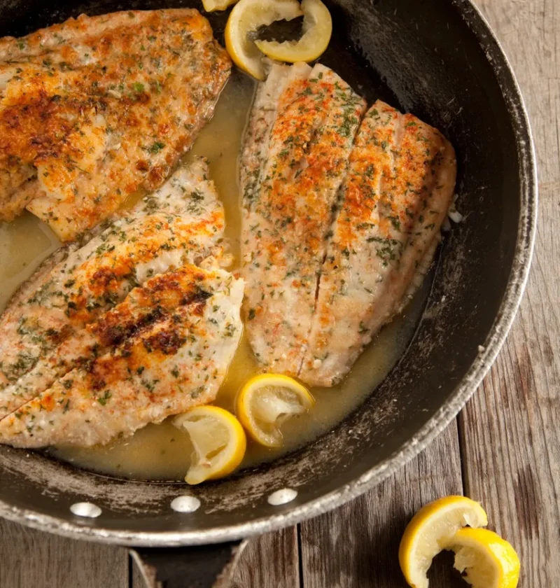 Paula Deen crab stuffed flounder fillets in a skillet with butter sauce and lemon wedges