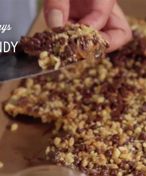 Paula Deen crack candy topped with mini chocolate chips and chopped nuts on a baking sheet, with a spatula lifting a piece