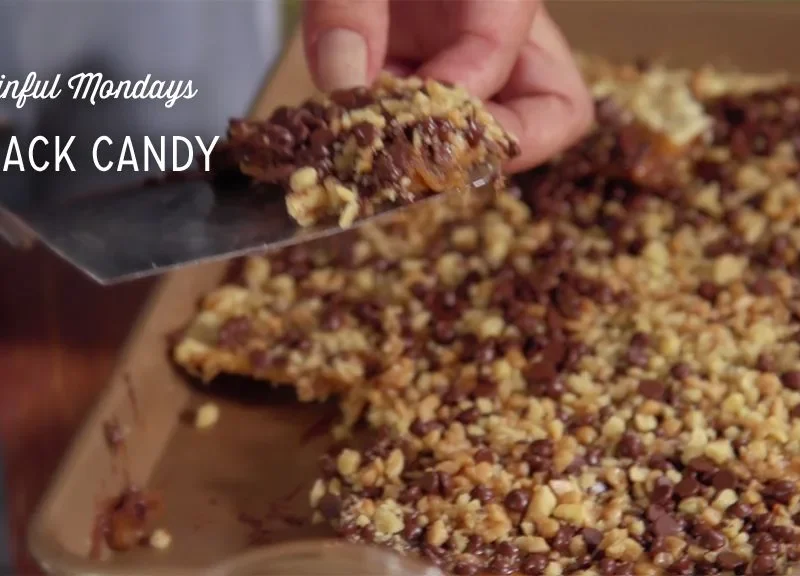 Paula Deen crack candy topped with mini chocolate chips and chopped nuts on a baking sheet, with a spatula lifting a piece