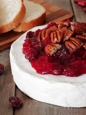 Paula Deen cranberry and pecan baked brie topped with cranberry sauce and pecans beside slices of bread