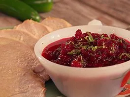 Paula Deen cranberry jalapeño relish in a white bowl next to sliced turkey and fresh jalapeños