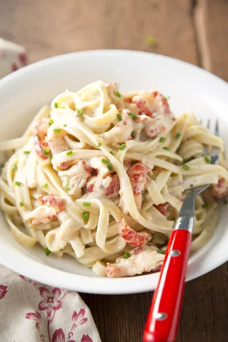 Paula Deen crawfish fettuccine in a white bowl with creamy sauce, crawfish tails and chopped chives, with a red-handled fork