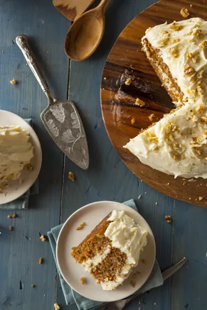 Paula Deen cream cheese frosting spread on a carrot cake topped with chopped pecans, with a slice on a plate