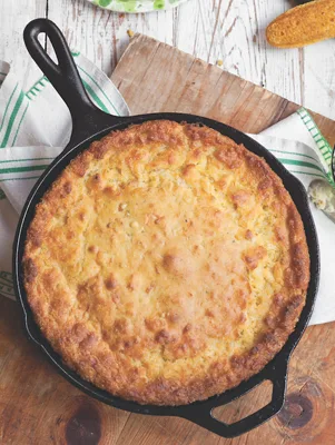 Paula Deen creamed corn cornbread baked golden brown in a 12-inch cast iron skillet on a wooden board
