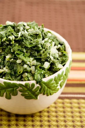 Paula Deen creamed spinach in a white bowl with a green leaf border, topped with soft diced onion