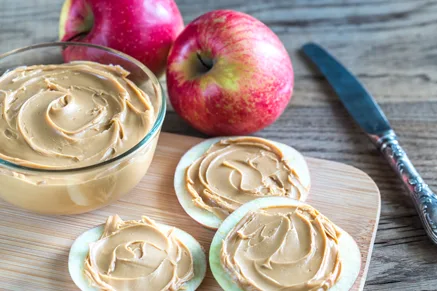 Paula Deen creamy apple butter swirled in a glass bowl and spread on apple slices beside fresh red apples