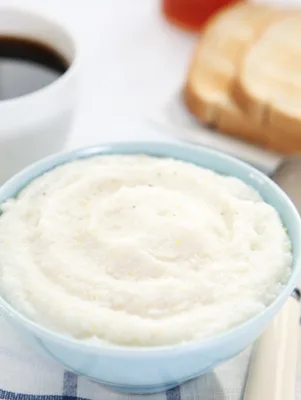 Paula Deen creamy grits in a light blue bowl with a cup of coffee and toast in the background