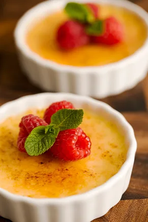Paula Deen creme brulee in white ramekins with a caramelized sugar top, fresh raspberries and a mint leaf