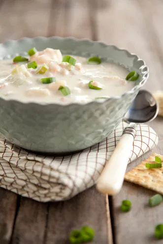Paula Deen Creole shrimp and lobster bisque in a scalloped bowl topped with sliced green onions beside a spoon and crackers