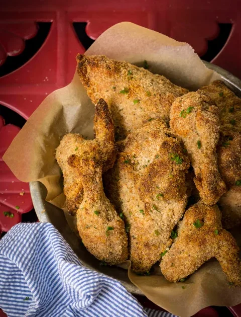 Paula Deen crispy oven-fried chicken pieces with golden bread crumb crust and green chive flecks in a parchment-lined bowl