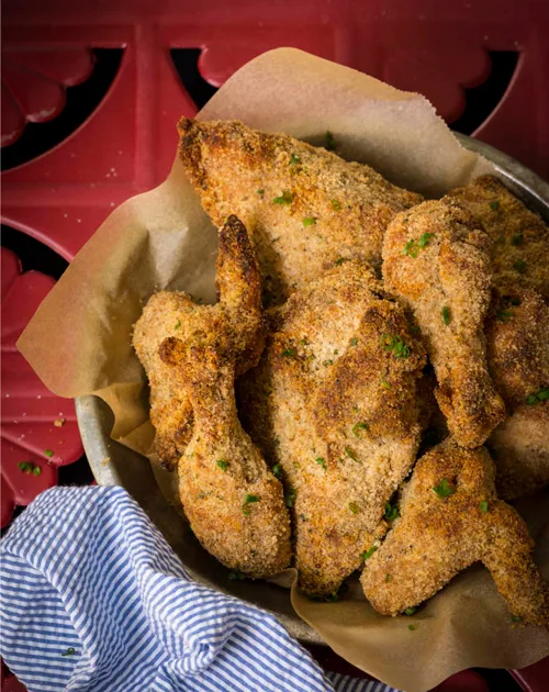 Paula Deen crispy oven-fried chicken pieces with golden bread crumb crust and green chive flecks in a parchment-lined bowl